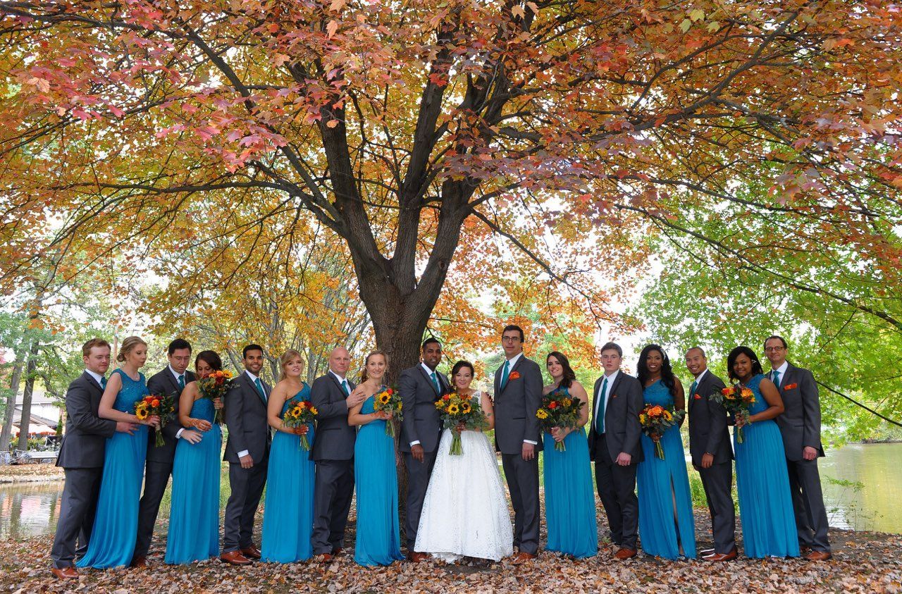 A bride and groom pose with their wedding party under a tree.