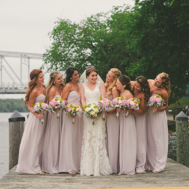 A bride and her bridesmaids are posing for a picture on a dock.