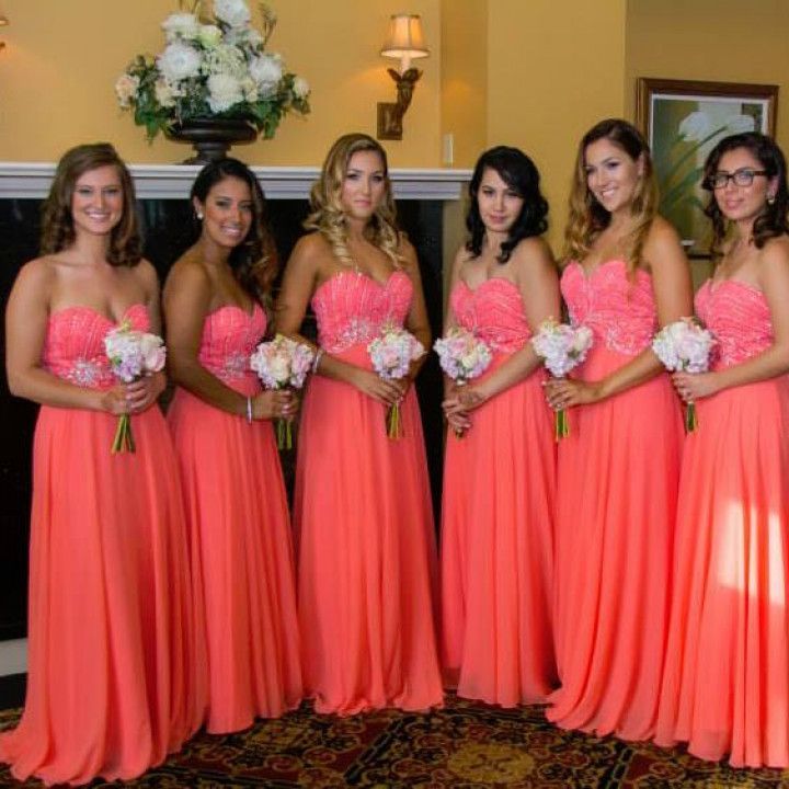 A group of women in coral dresses are posing for a picture