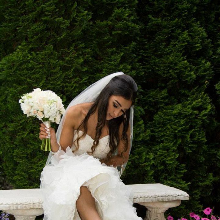 A bride is sitting on a bench holding a bouquet of flowers