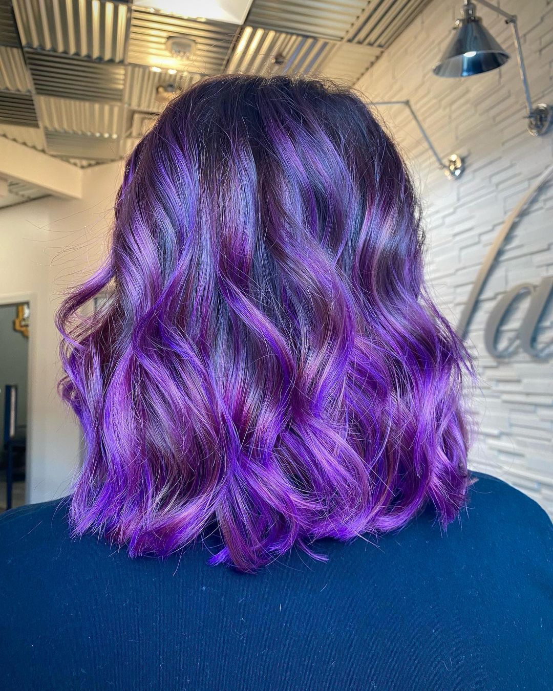 a woman with purple hair is standing in front of a wall that has the word la on it