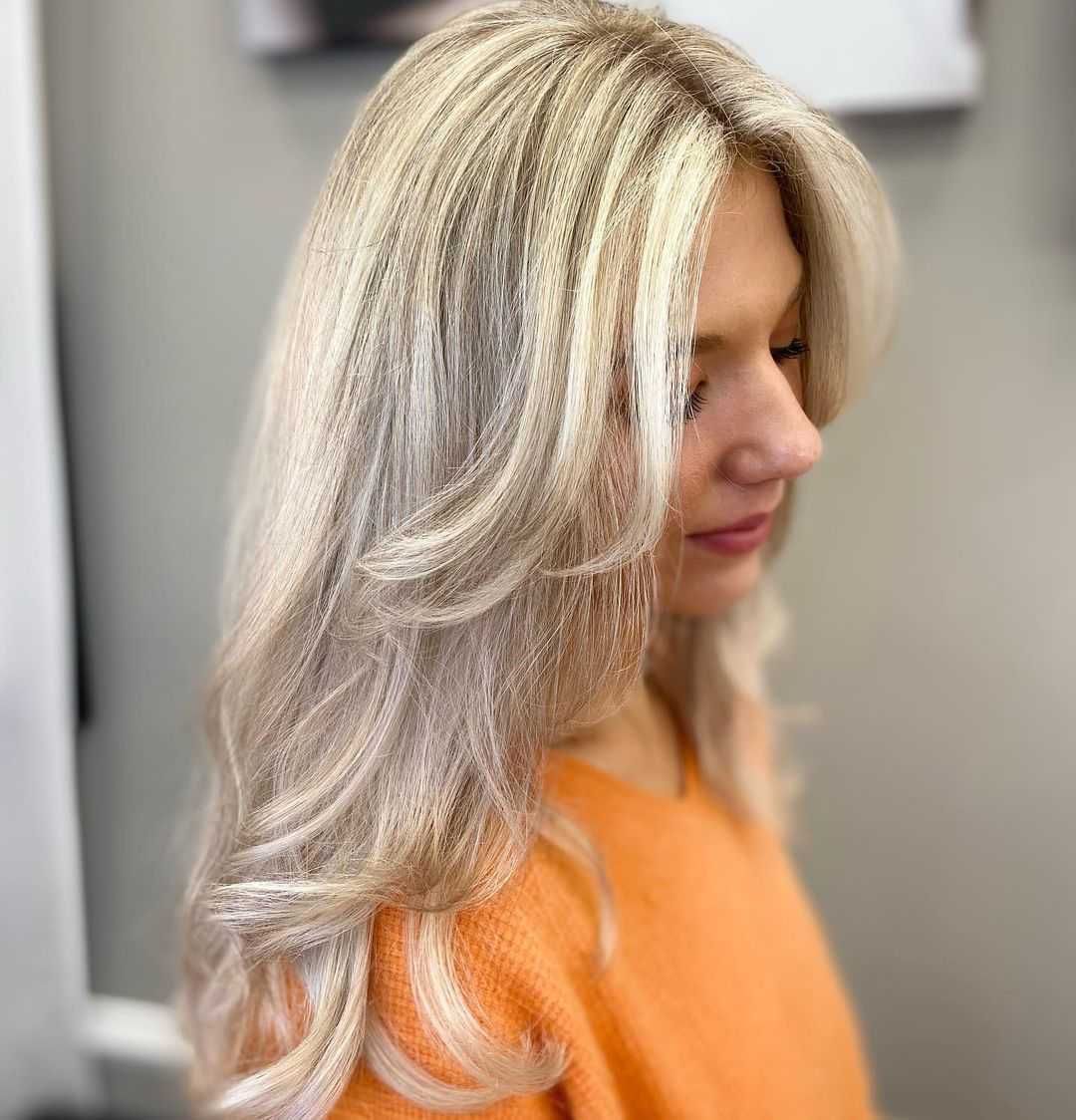 a woman with long blonde hair is wearing an orange sweater .