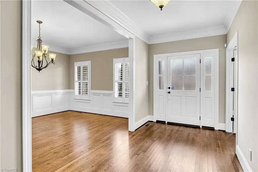 An empty room with hardwood floors and a chandelier hanging from the ceiling.