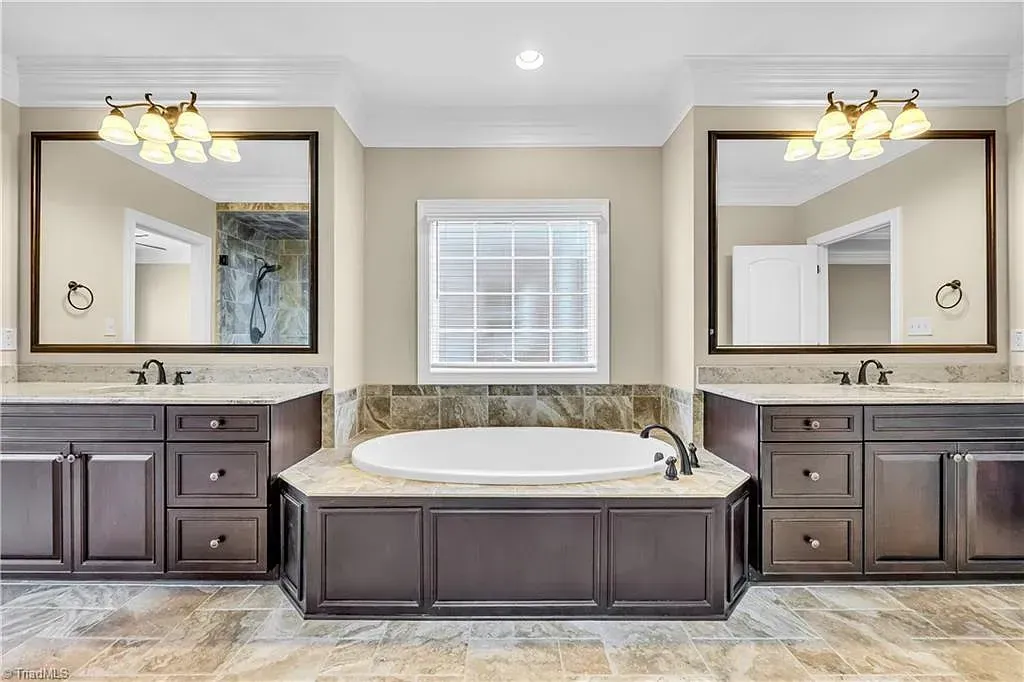 A bathroom with two sinks , a tub , and two mirrors.