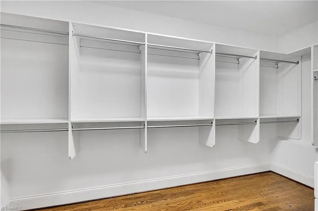 An empty walk in closet with white shelves and wooden floors.