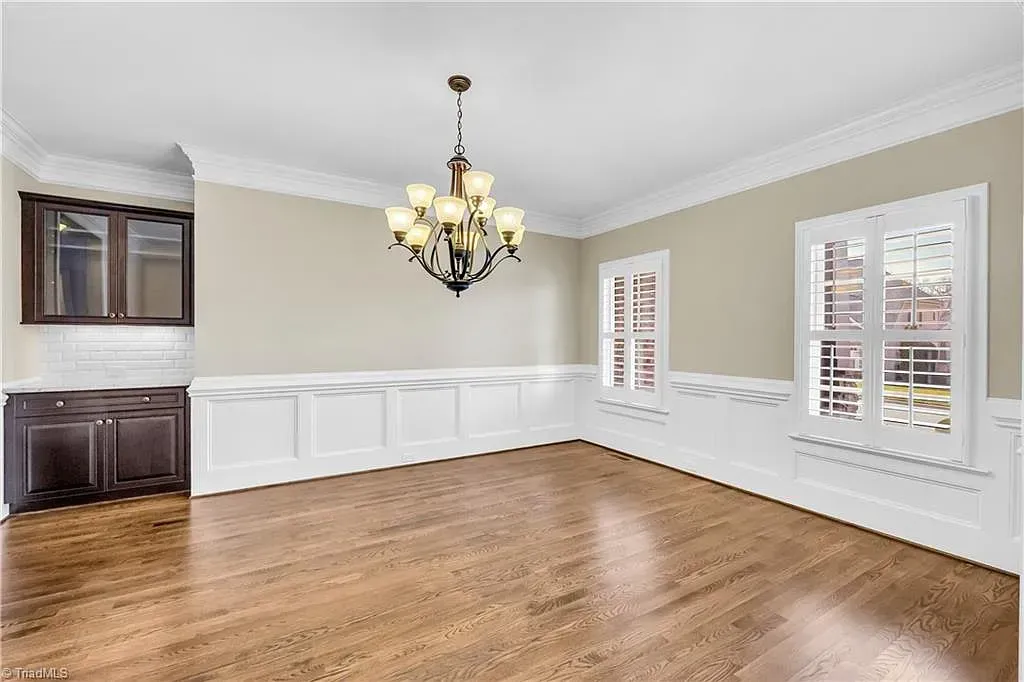 An empty dining room with hardwood floors and a chandelier hanging from the ceiling.