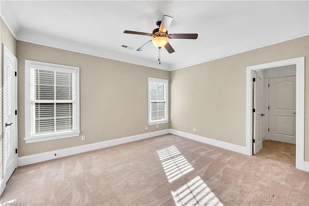 An empty bedroom with a ceiling fan and two windows.