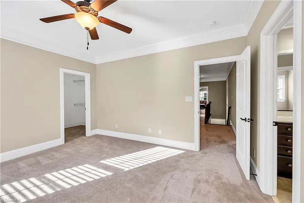 An empty bedroom with a ceiling fan and a carpeted floor.