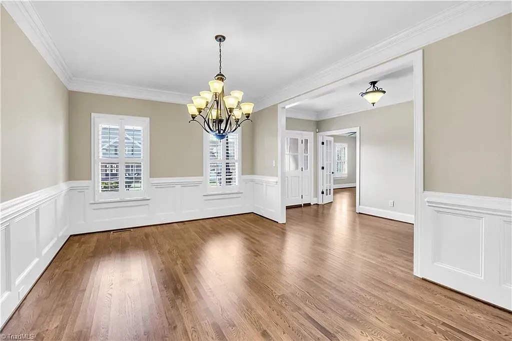 An empty living room with hardwood floors and a chandelier hanging from the ceiling.