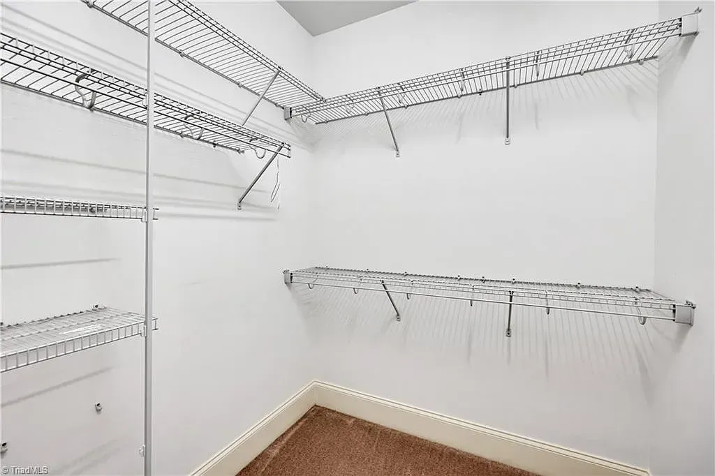 A walk in closet with lots of shelves and a brown carpet.
