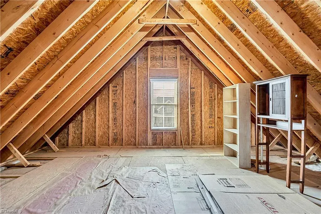 An attic in a house under construction with wooden beams and a window.