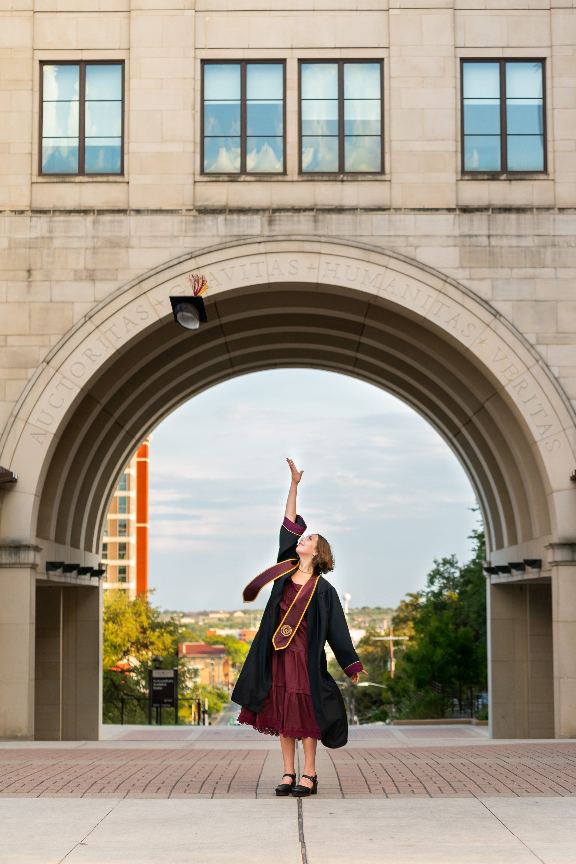 A woman in a graduation cap and gown is throwing her cap in the air.