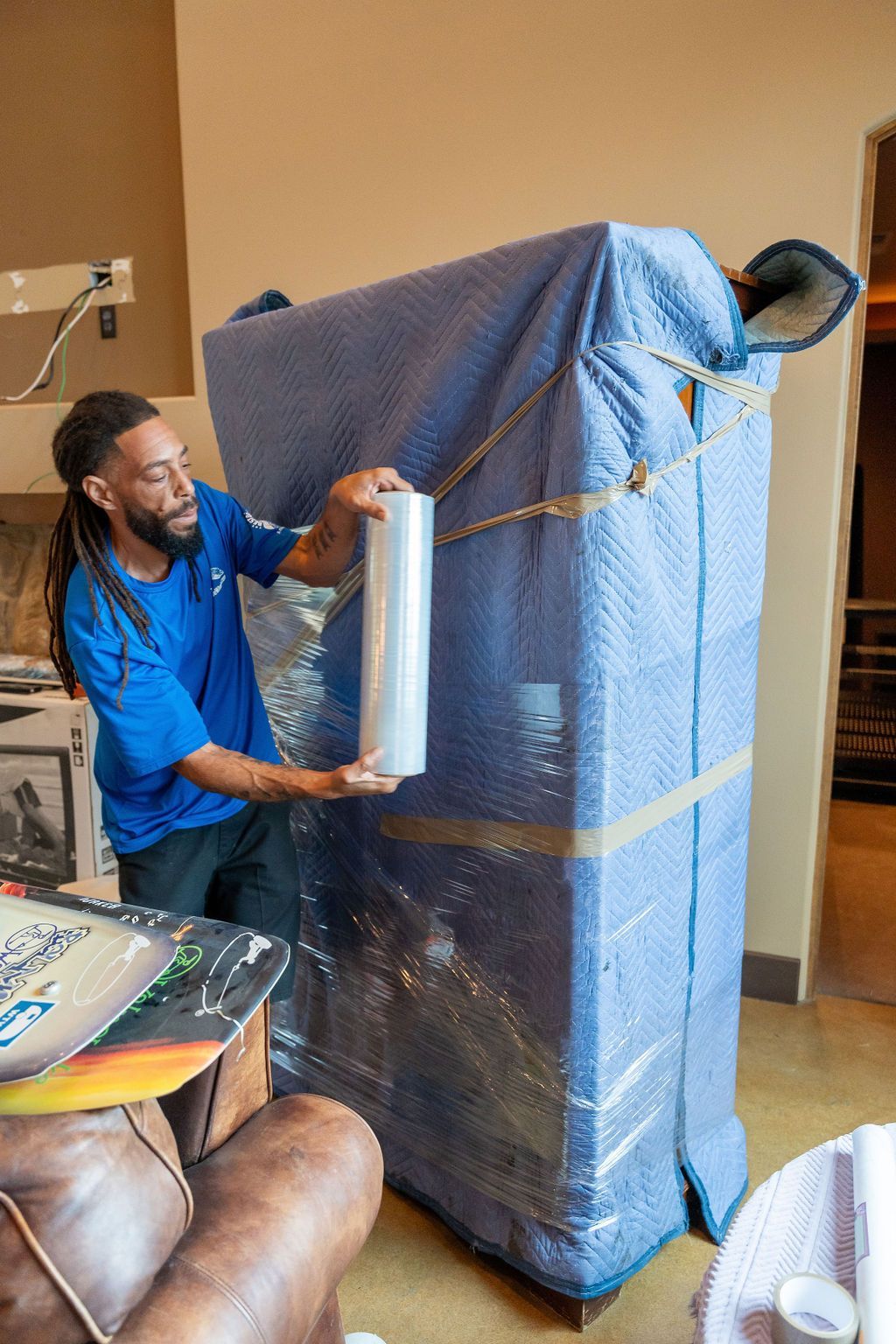 A man is wrapping a refrigerator with plastic wrap in a living room.