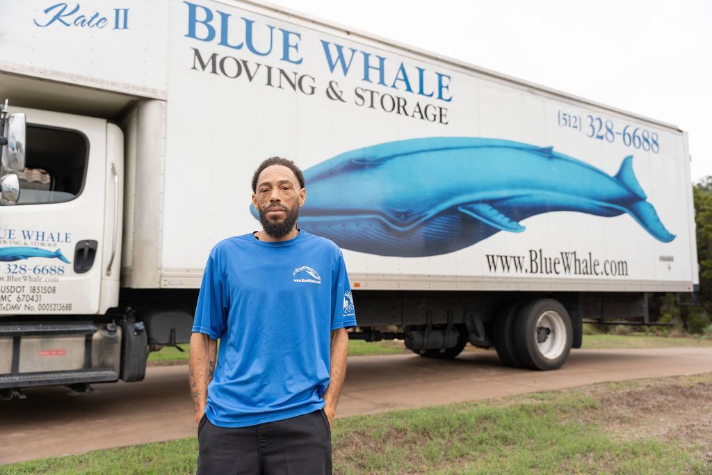 A man is standing in front of a blue whale moving and storage truck.