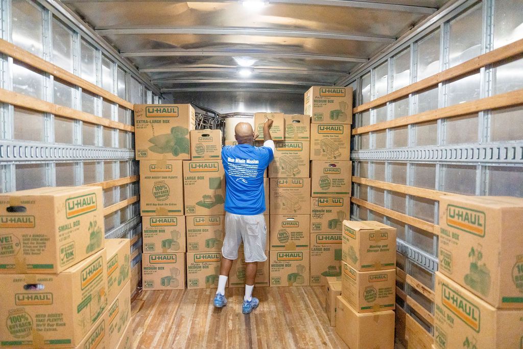 A man is standing in the back of a moving truck filled with boxes.