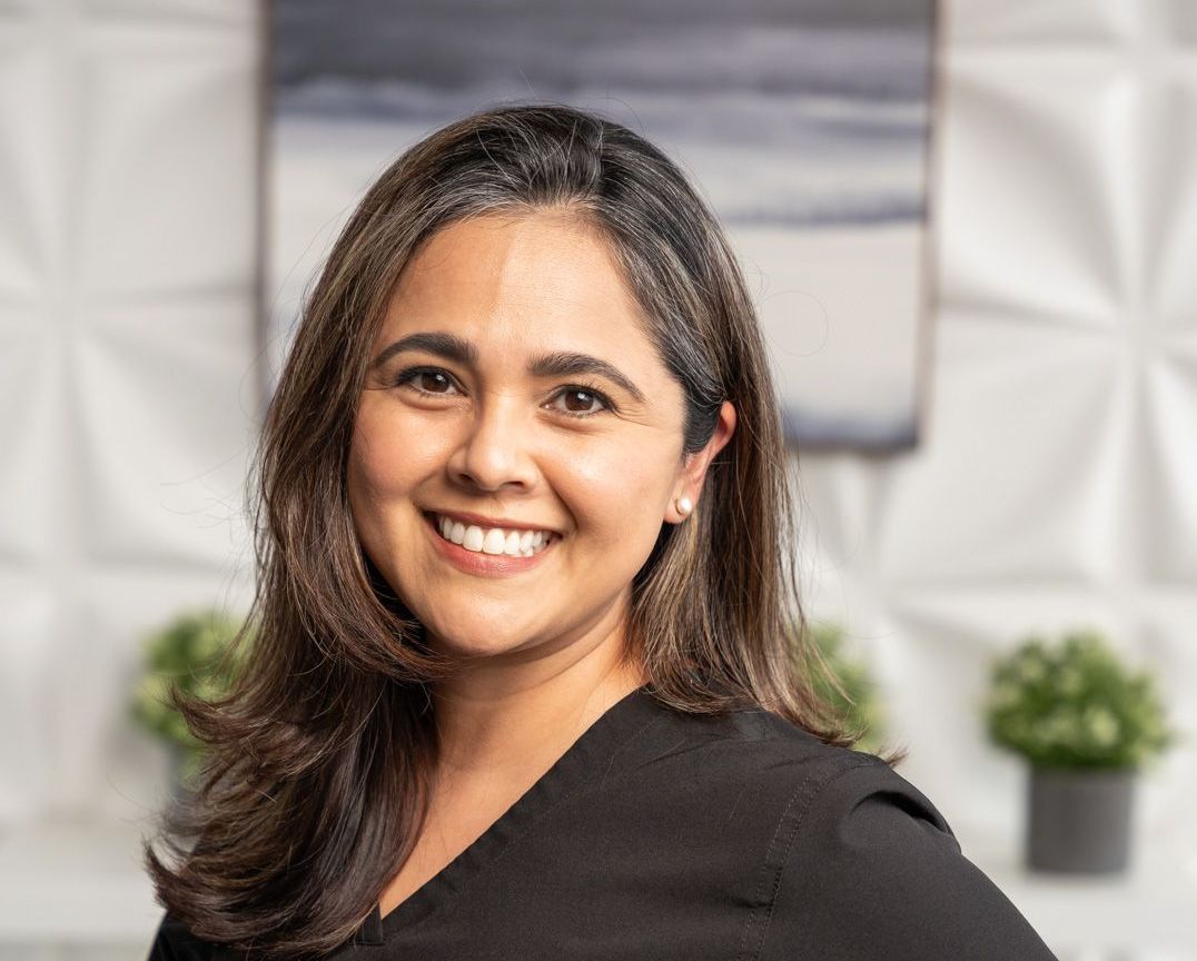 A woman in a black scrub top is smiling for the camera.