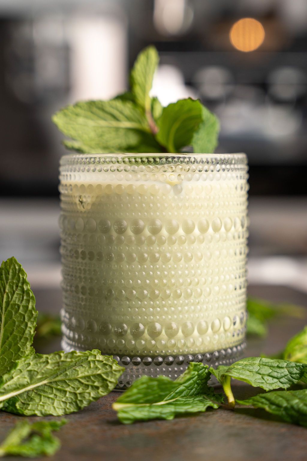 A close up of a drink in a glass with mint leaves on a table.