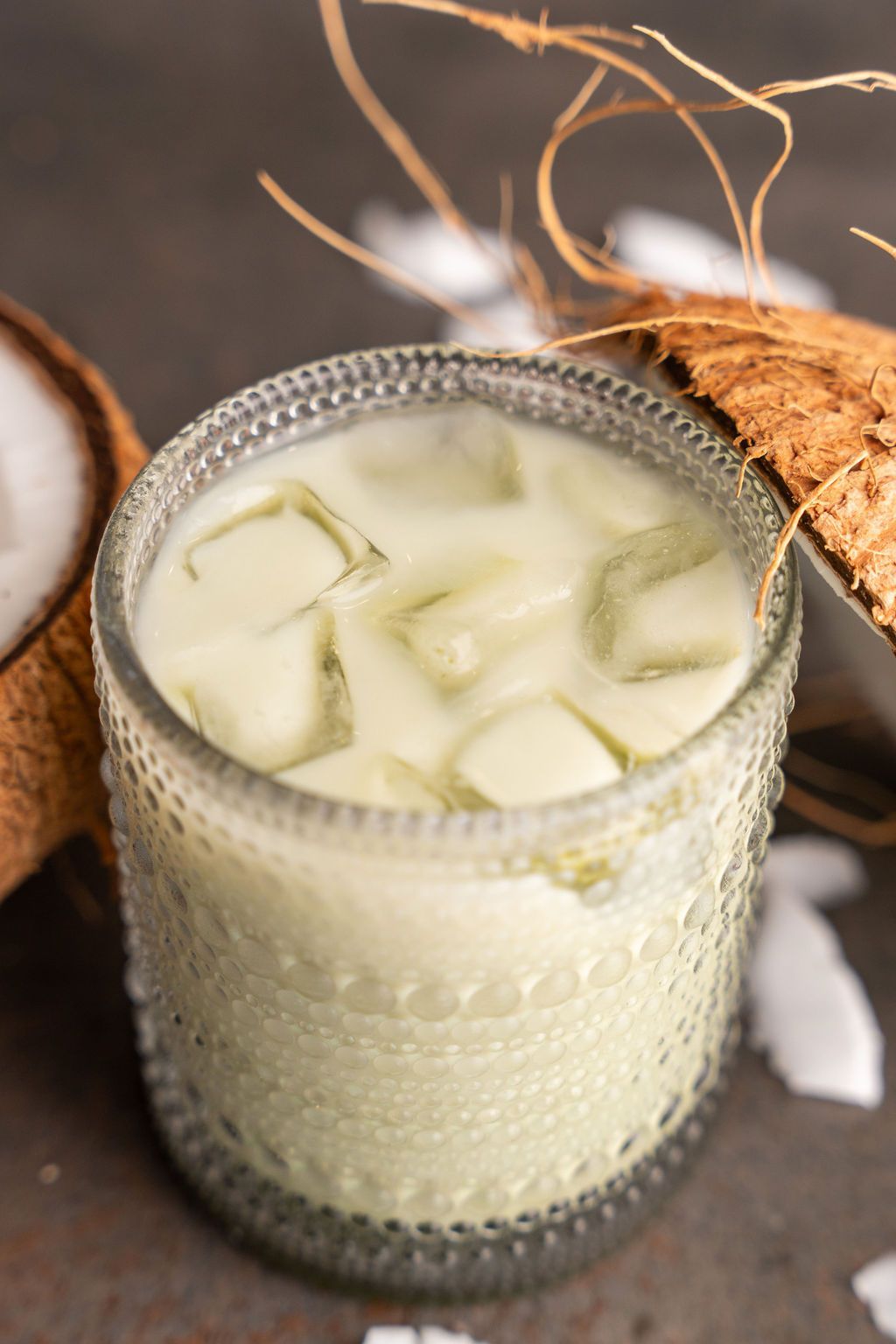 A close up of a glass of coconut milk with ice cubes.