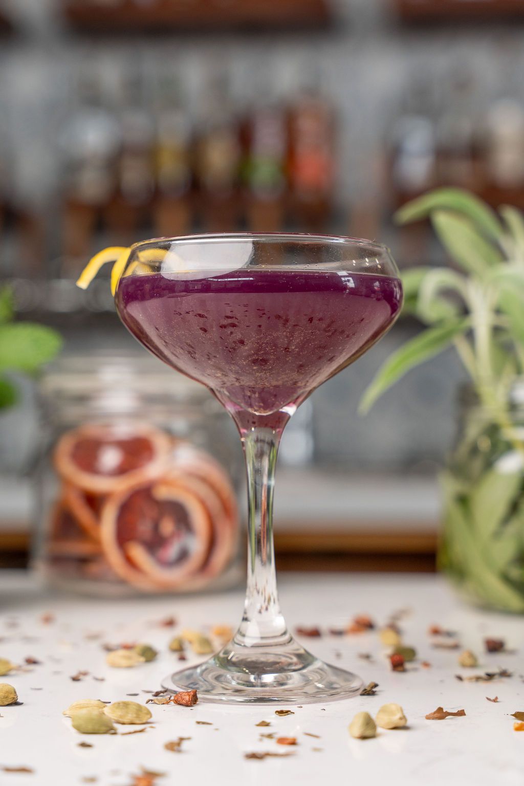 A close up of a purple cocktail in a martini glass on a table.