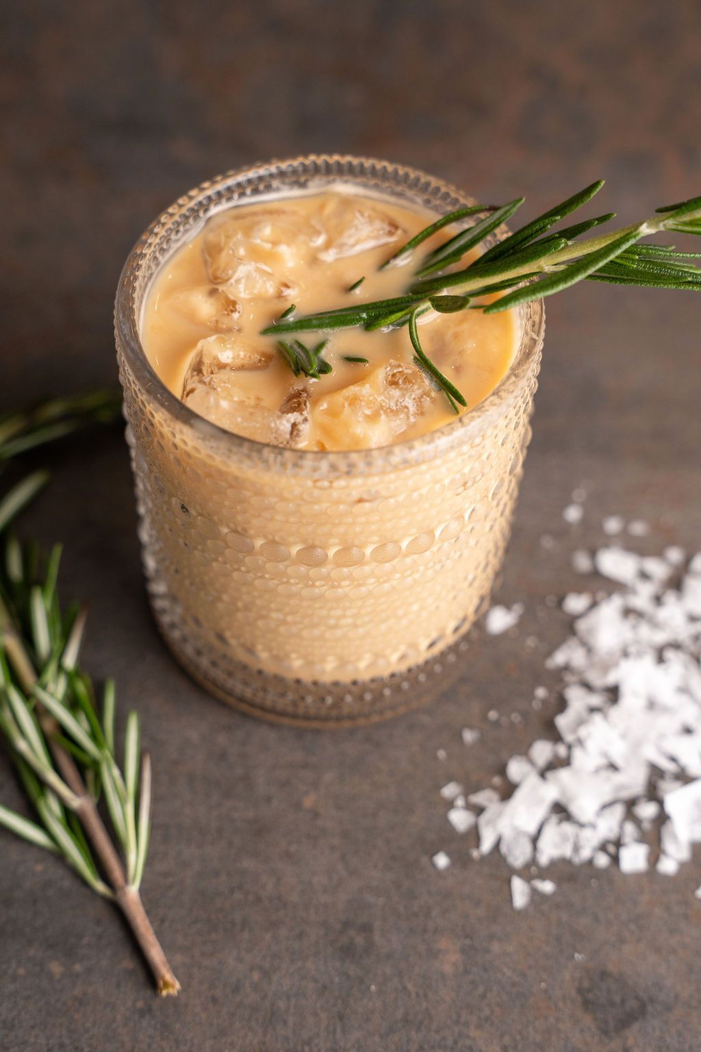 A close up of a glass of soup with a sprig of rosemary on top.