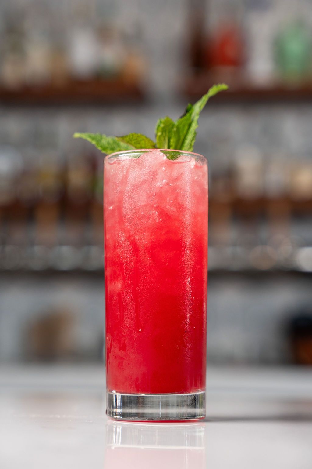 A close up of a red drink in a tall glass on a table.