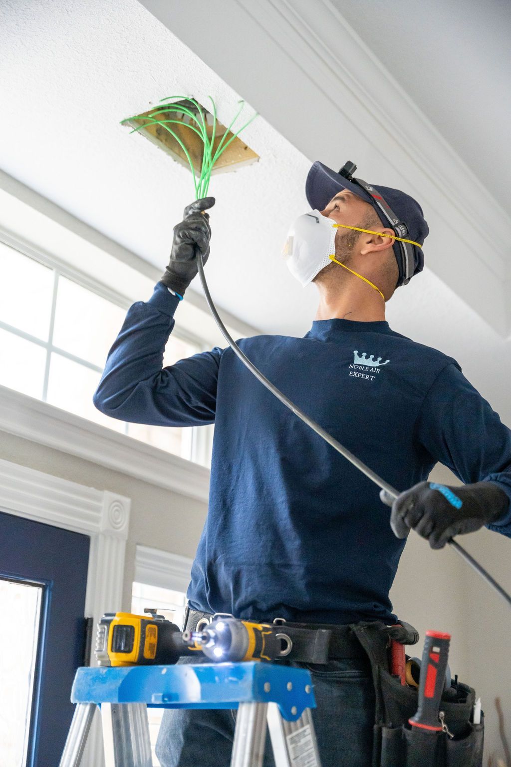 A man wearing a mask is standing on a ladder cleaning a ceiling.