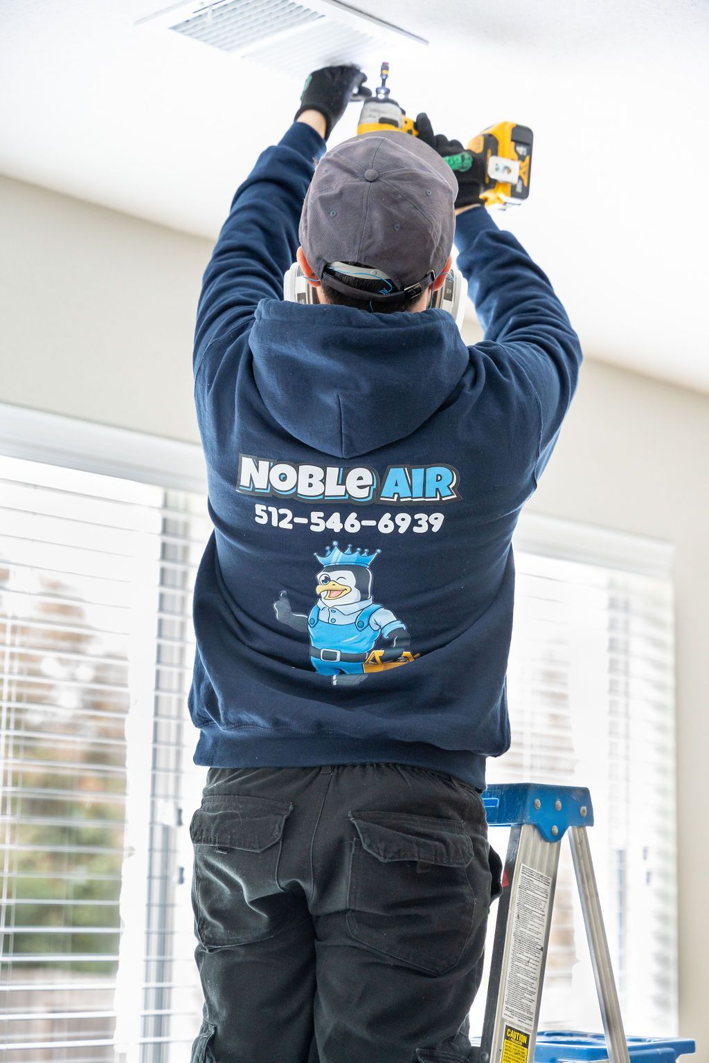 A man is standing on a ladder working on a ceiling fan.