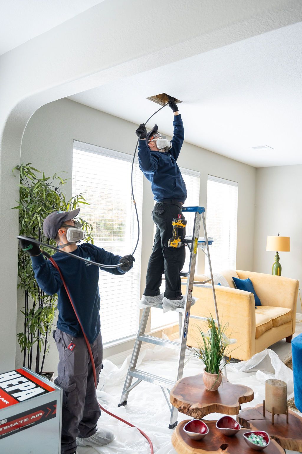 Two men are working on a ceiling in a living room.