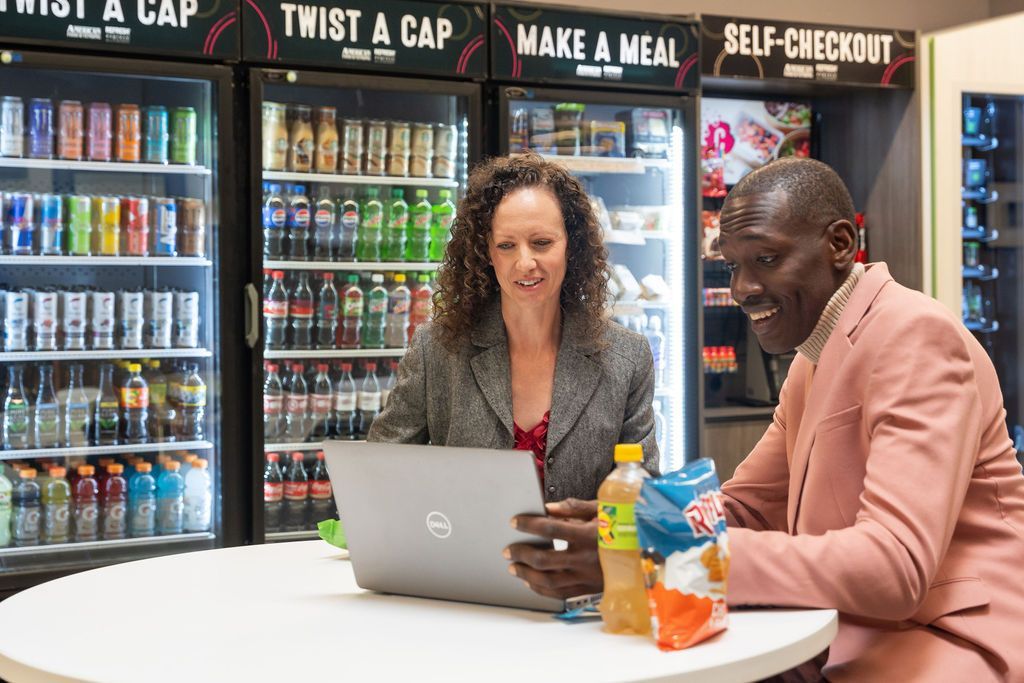 A man and a woman are sitting at a table looking at a laptop.