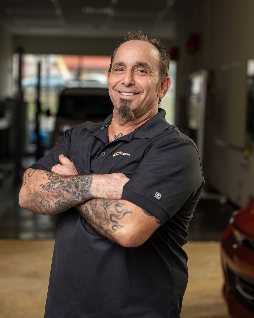 A man with tattoos on his arms is standing in a garage with his arms crossed.