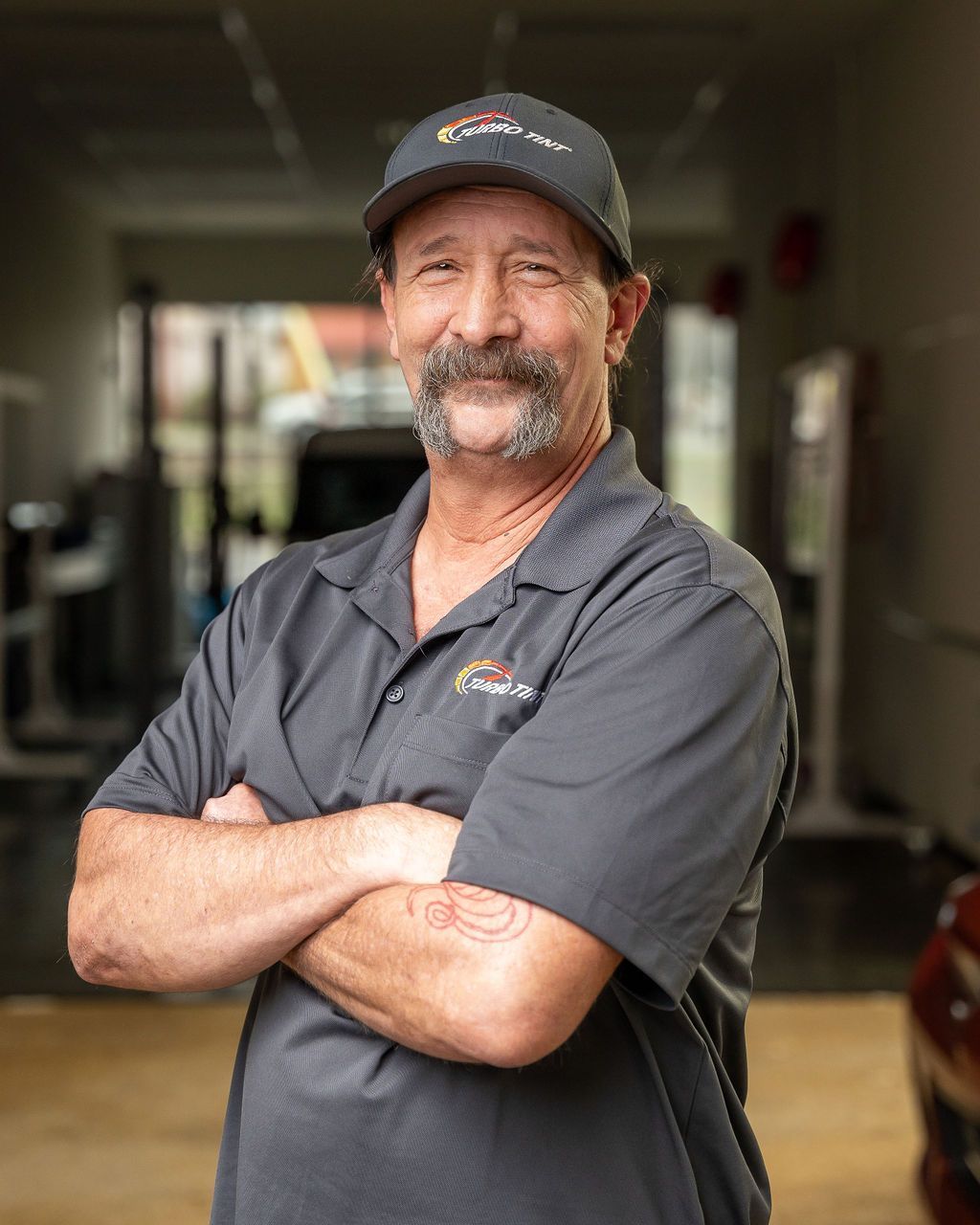 A man with a beard and mustache is standing with his arms crossed in a gym.