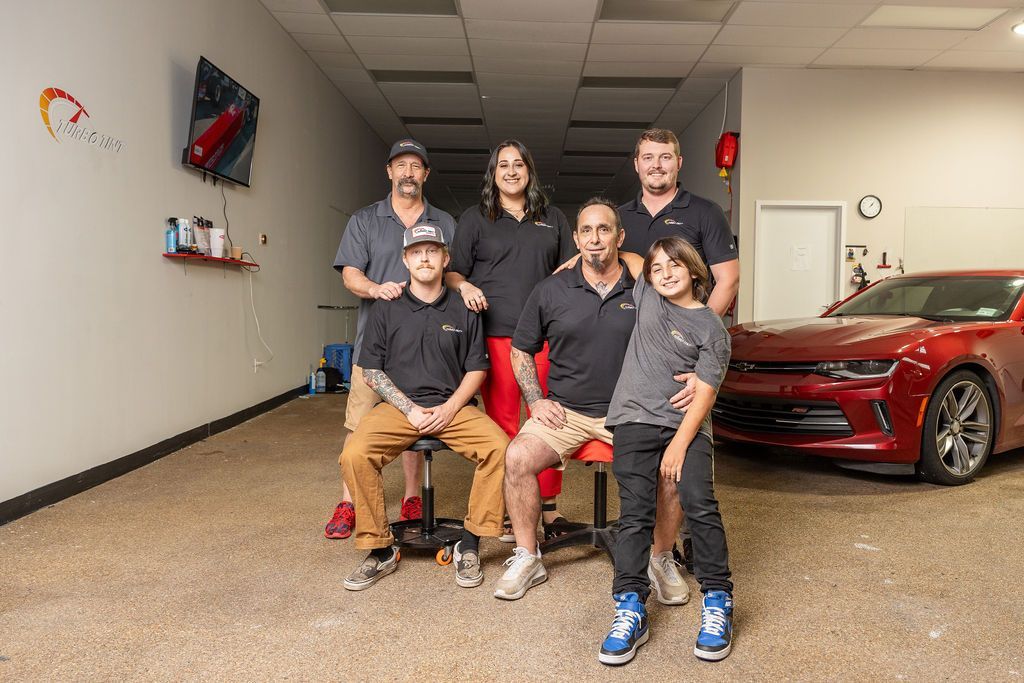 A group of people are posing for a picture in front of a red car.