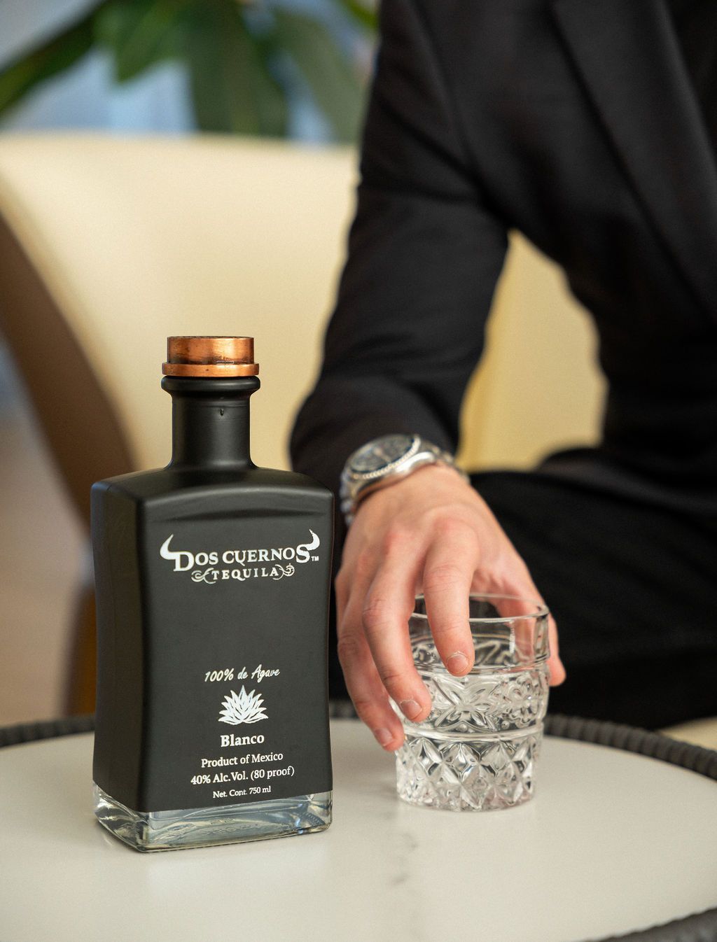 A man is holding a glass of water next to a bottle of tequila