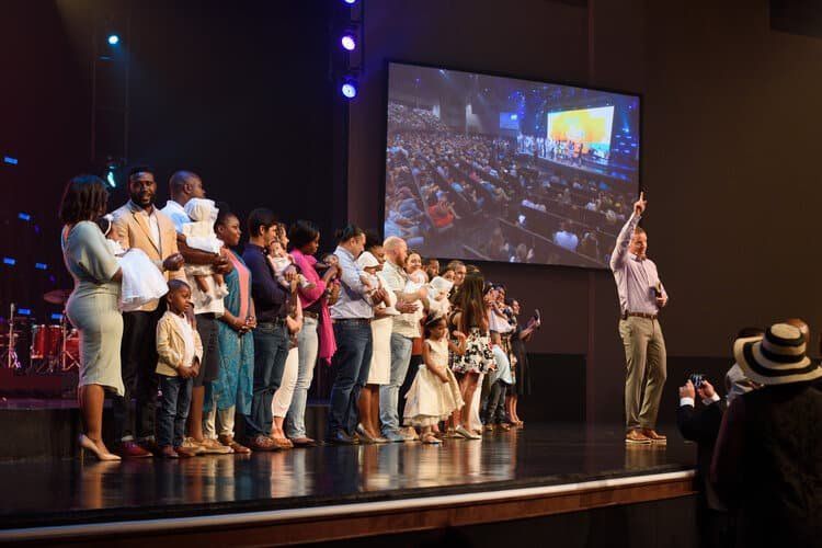 A group of people are standing on a stage in front of a large screen.