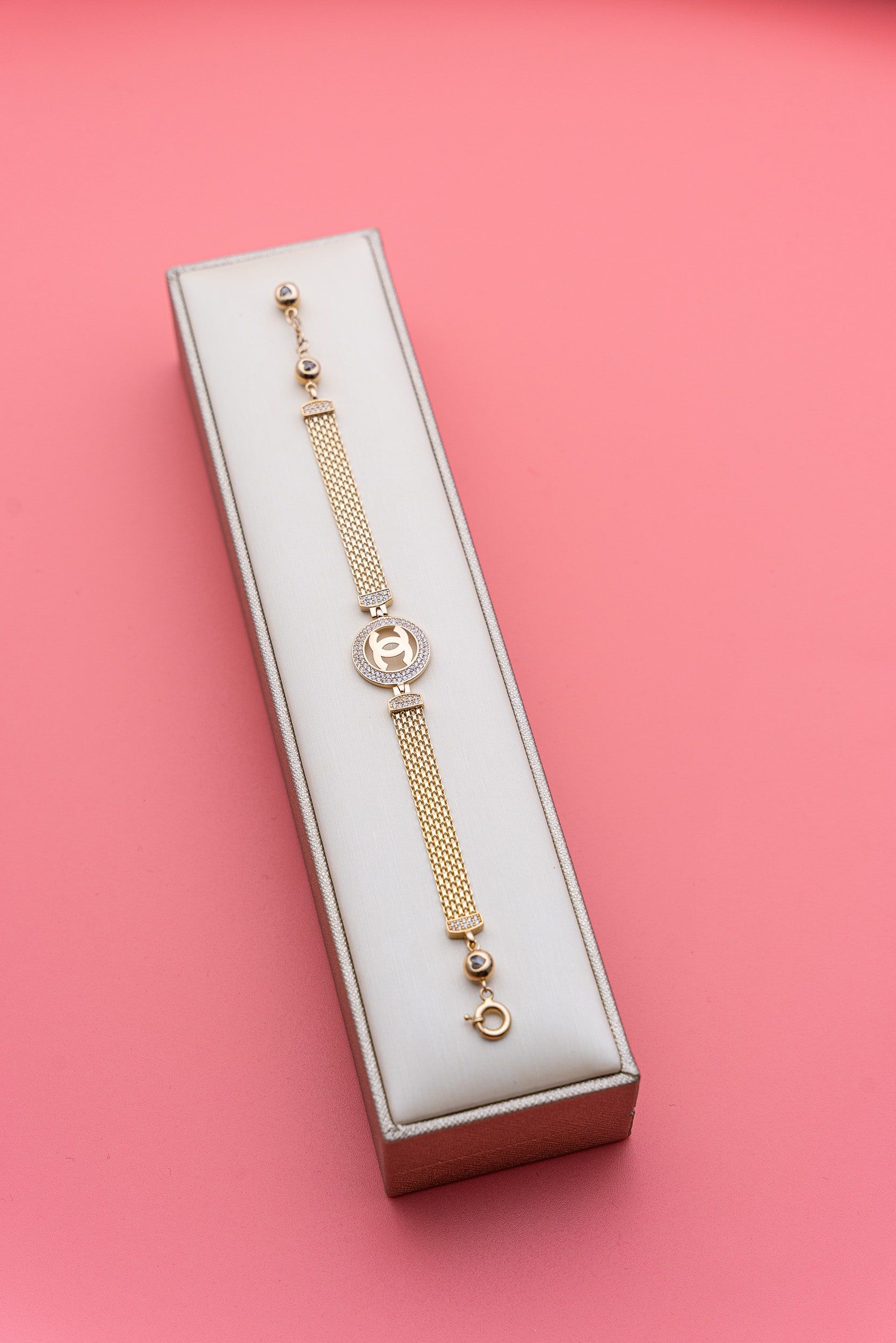 A gold bracelet is sitting in a white box on a pink surface.