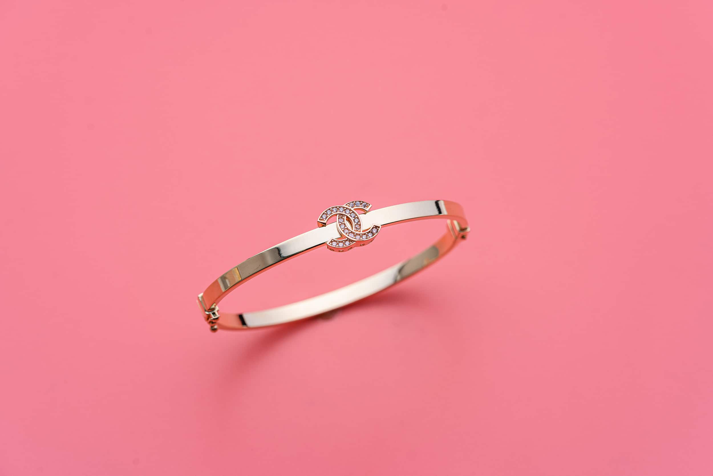 A gold bracelet with a diamond on a pink background.