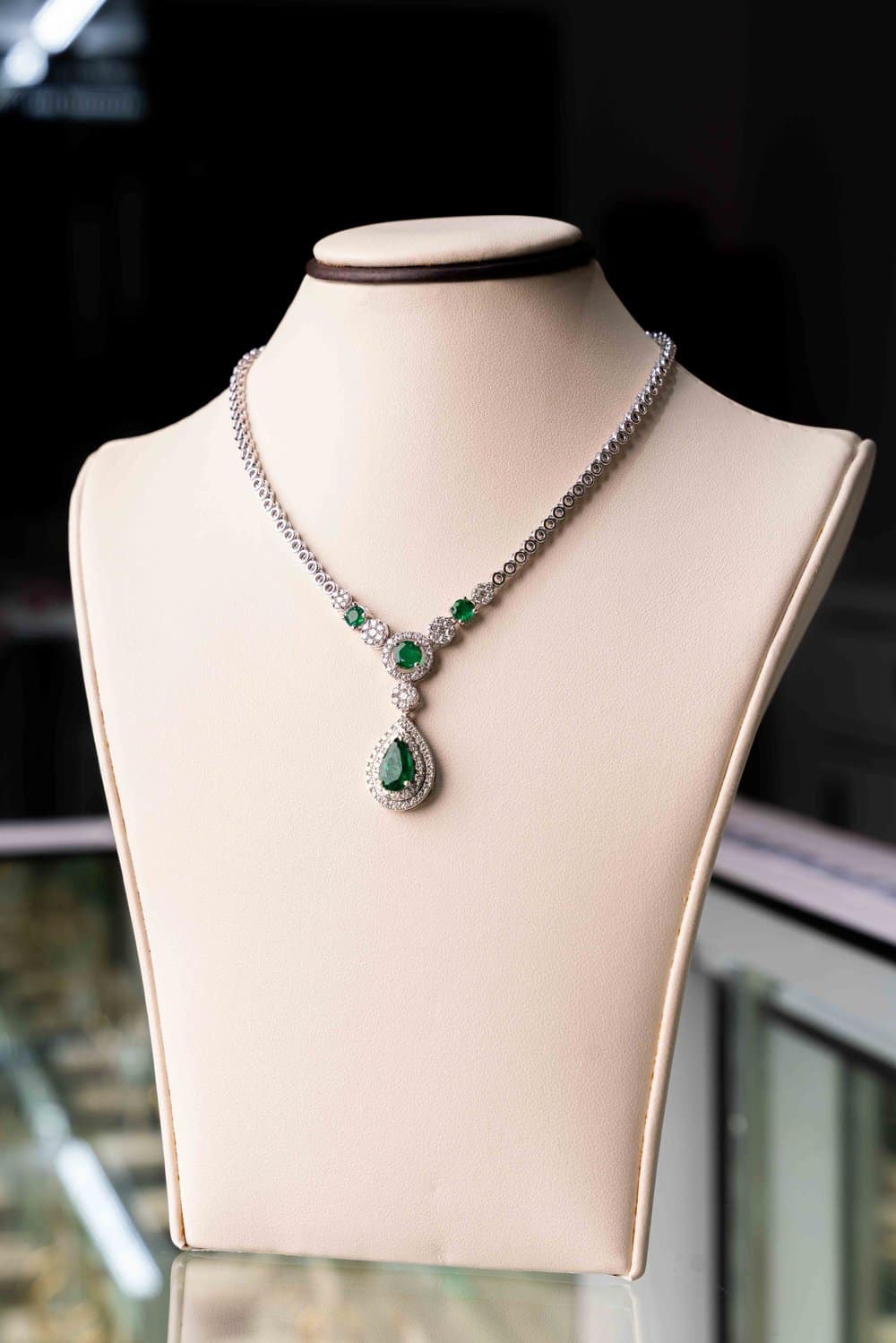 A necklace with emeralds and diamonds is on a mannequin.