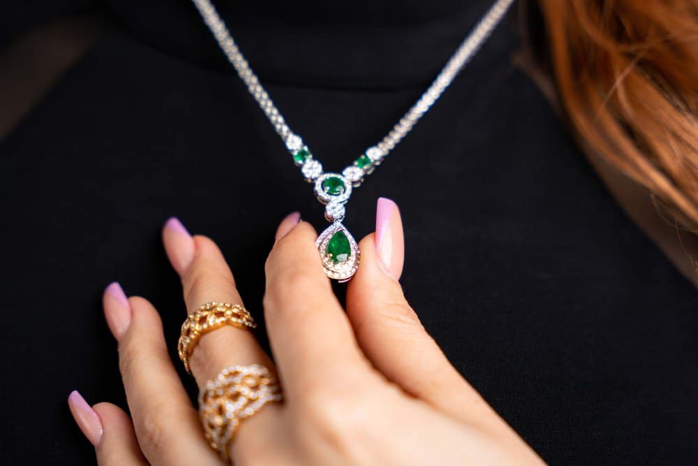 A woman is wearing a necklace with emeralds and diamonds.