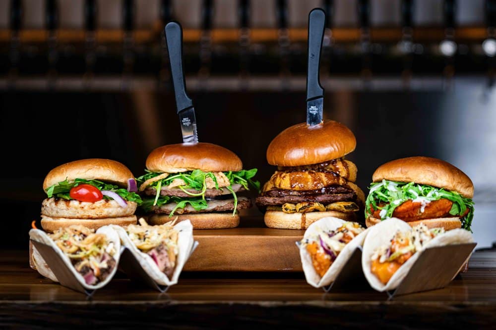 A tray of burgers and tacos on a wooden table.