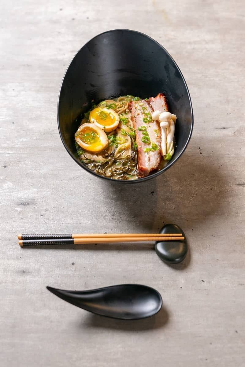 A bowl of food with chopsticks and a spoon on a table.