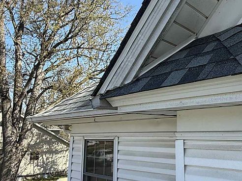 White house exterior with gray shingle roof, gutters, and siding, and a bare tree in the background.