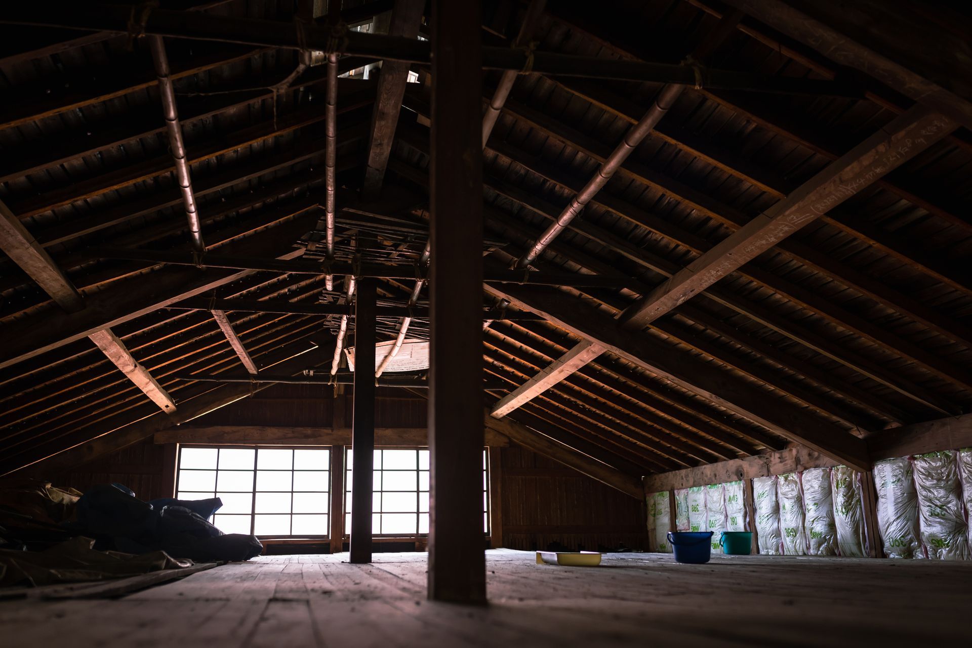 Person blowing insulation into an attic; wood beams, white insulation, blue shirt.