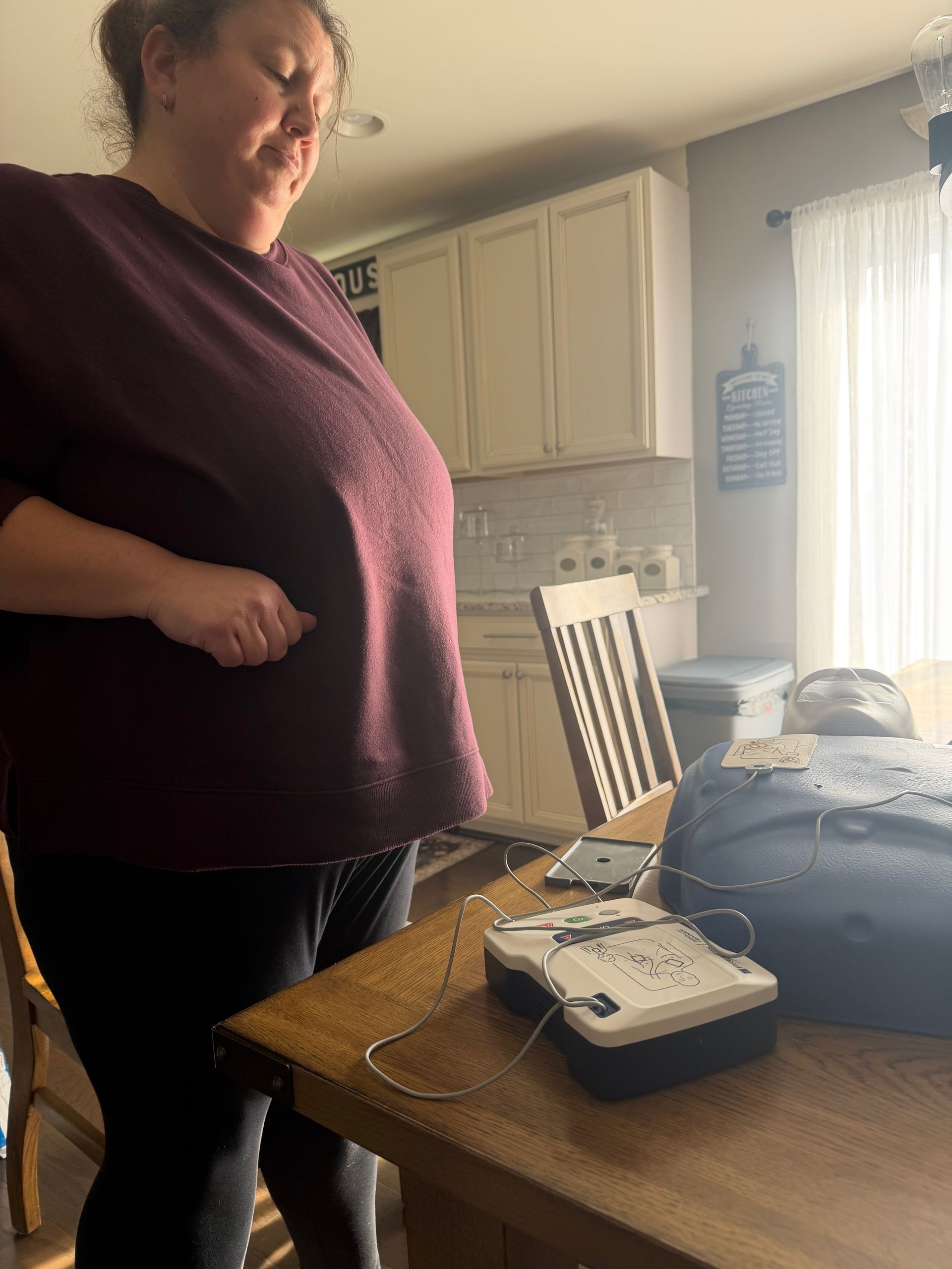 Woman next to a table with a medical device and a phone. Kitchen setting, overcast light.