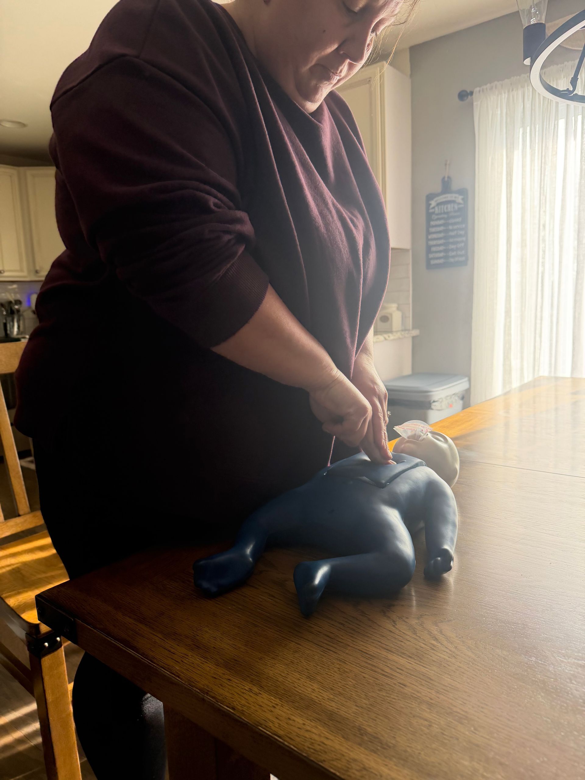 Woman performing CPR on a training dummy lying on a wooden table.