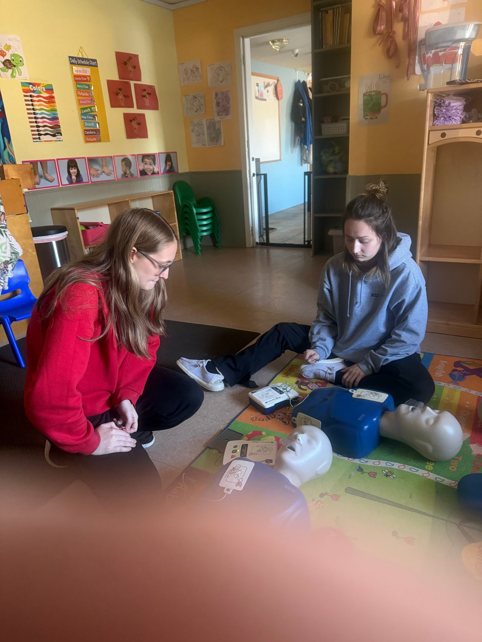 Two people practice CPR on mannequins indoors.