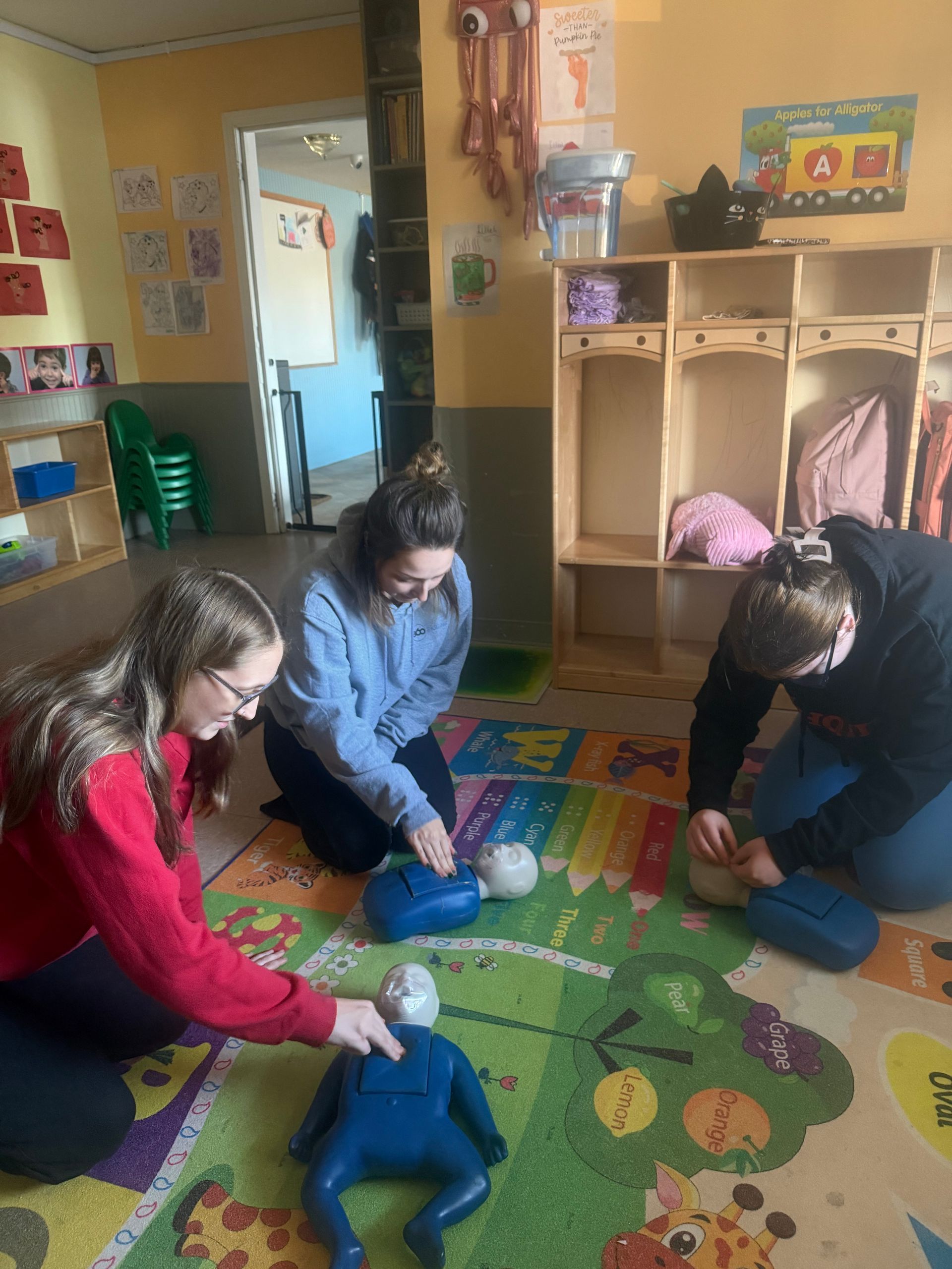 Three people practicing CPR on mannequins indoors.