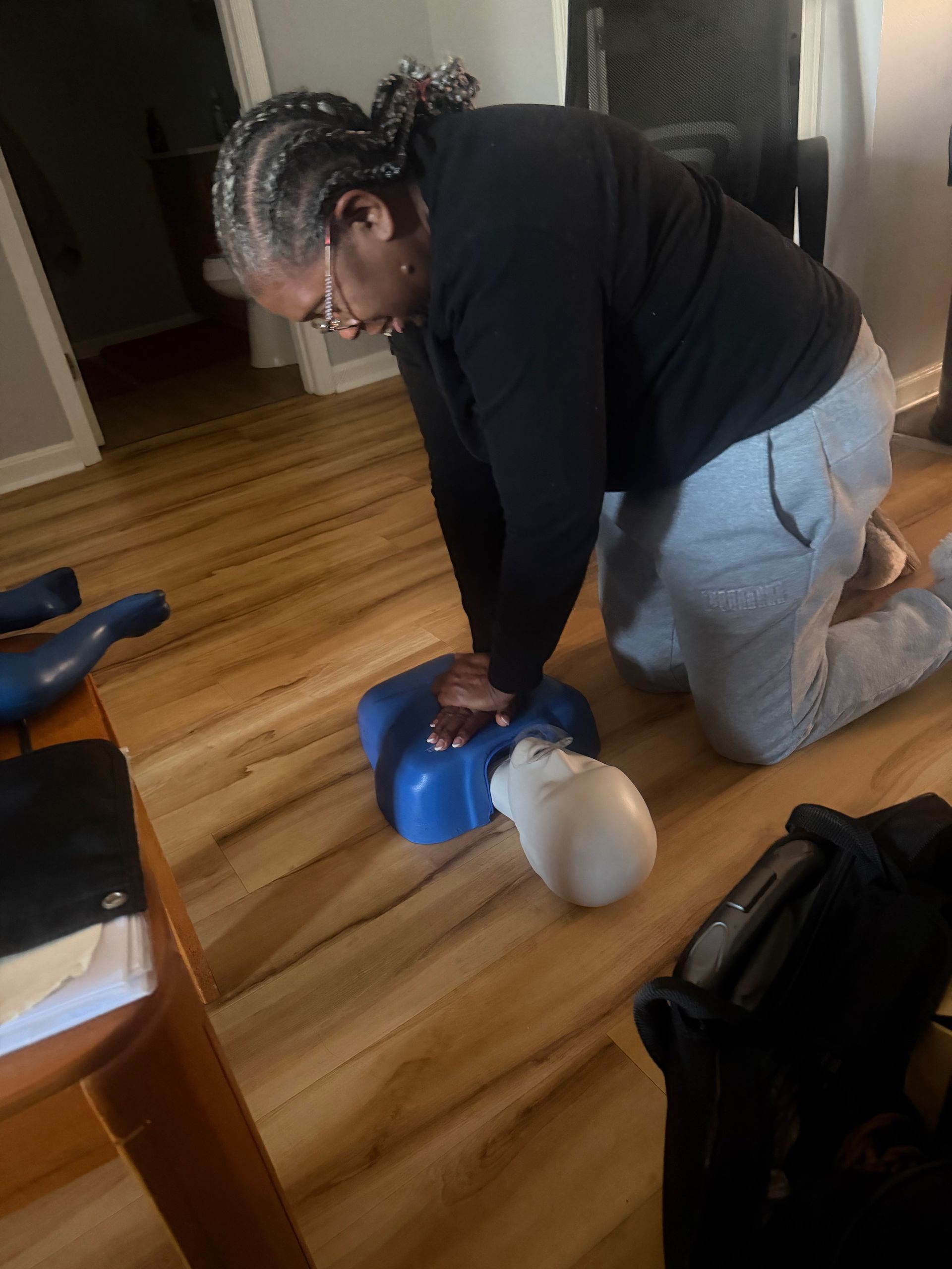 Person practicing CPR on a training dummy, kneeling on a wooden floor.