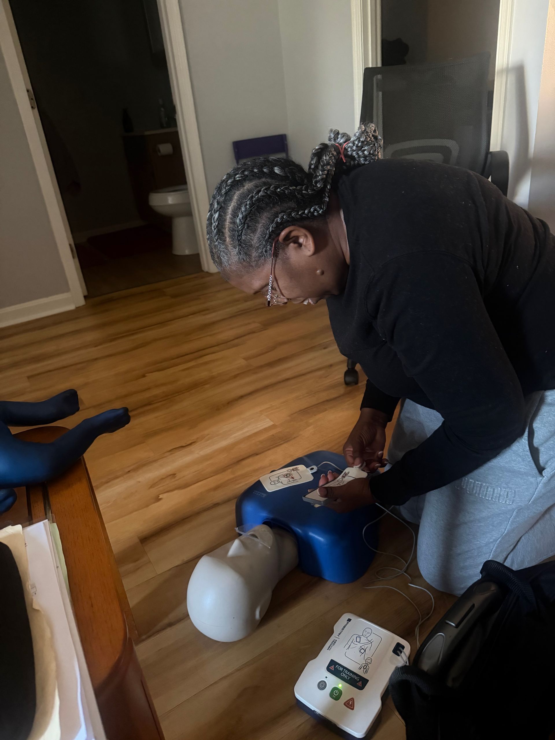 Woman practicing CPR on a training dummy with an AED device on the floor.
