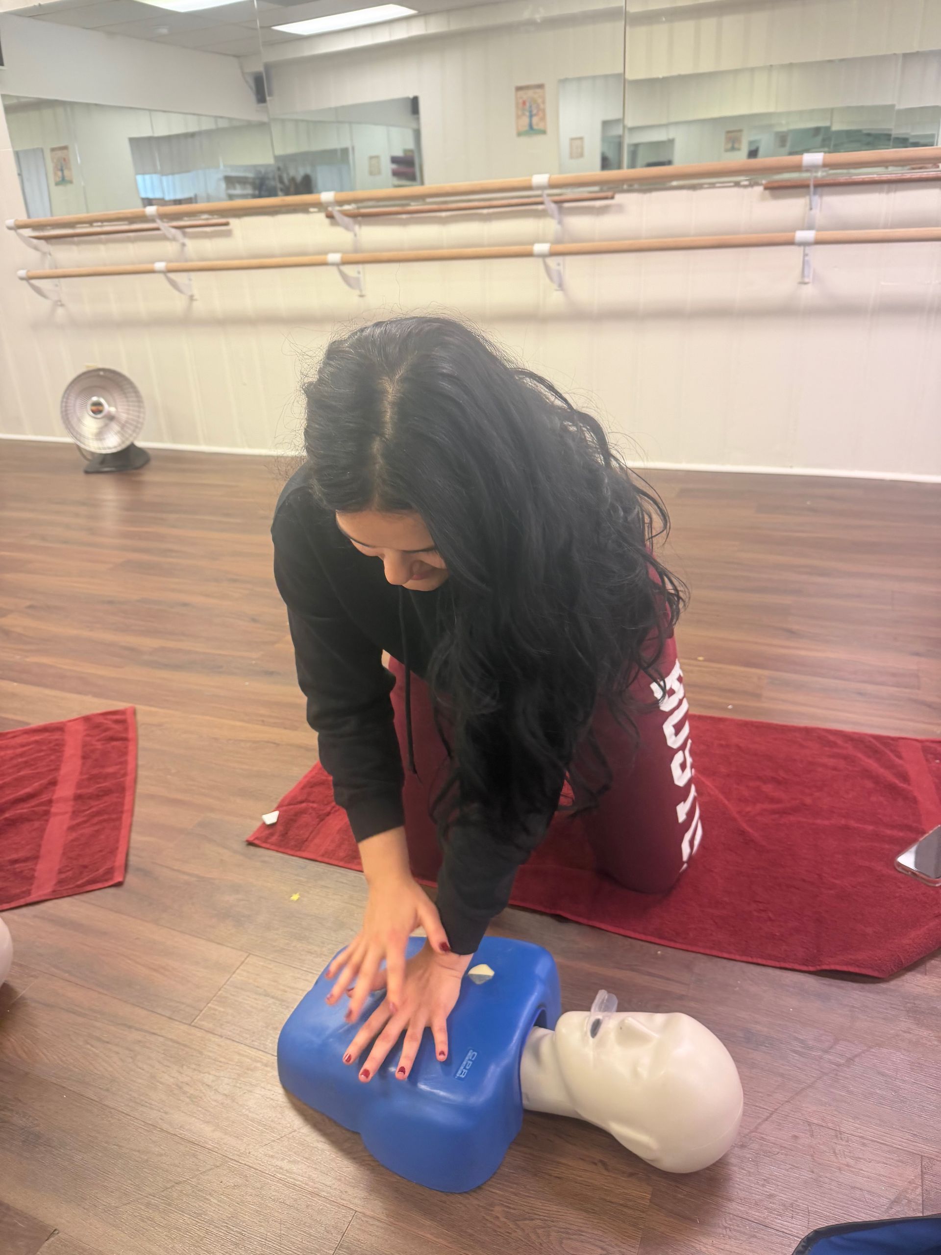 Woman practicing CPR on a training dummy, kneeling on a red towel in a studio.