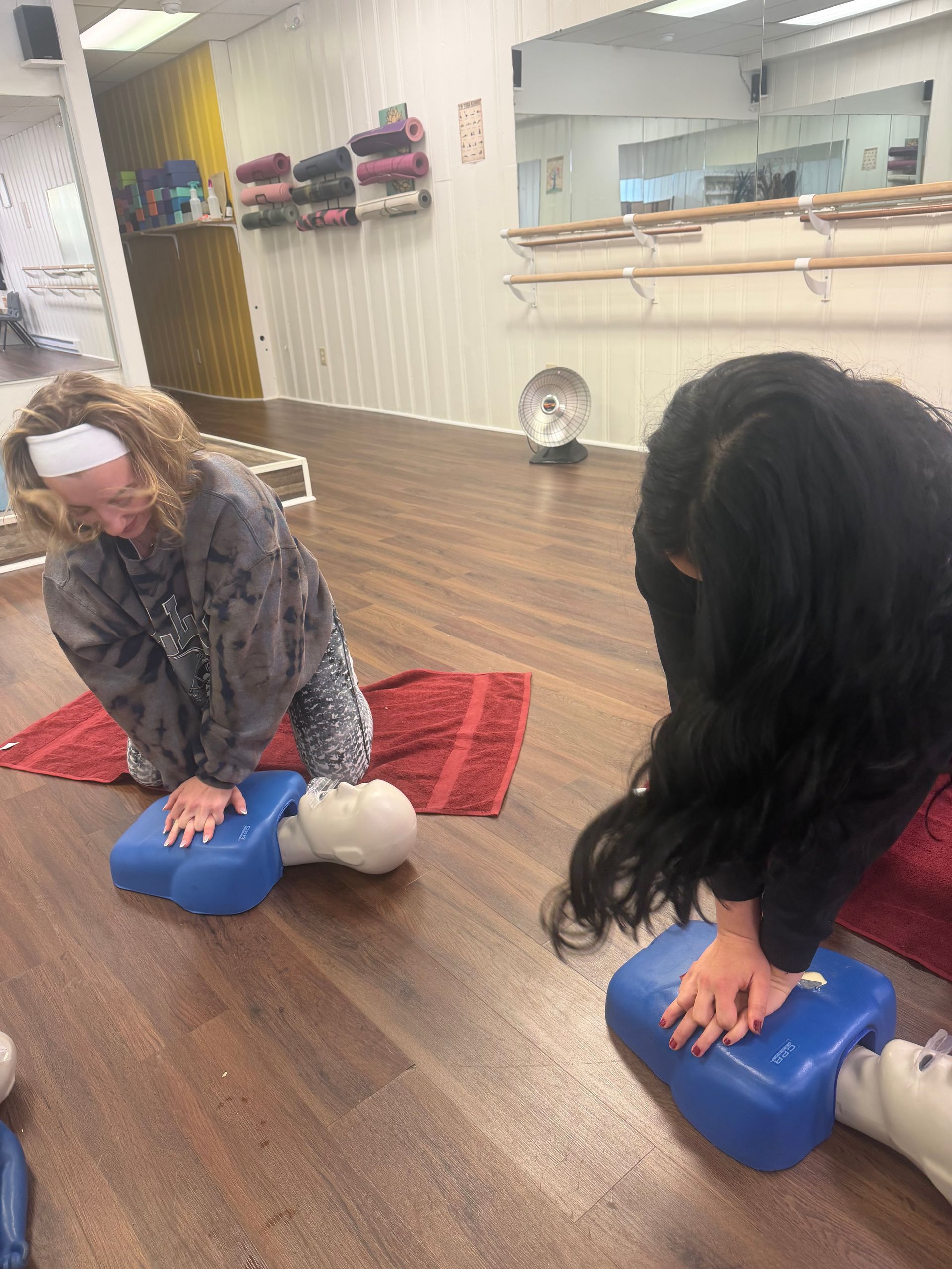 Two people practicing CPR on training mannequins in a studio.